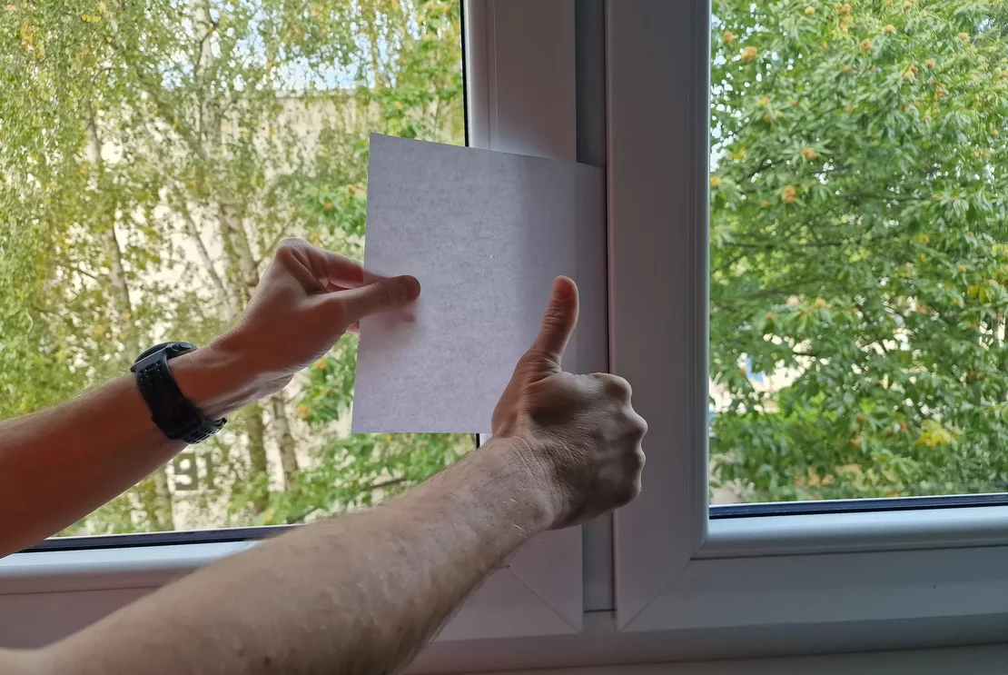 Orientačná kontrola prítlaku okenného krídla pomocou listu papiera vloženého medzi krídlo a rám.